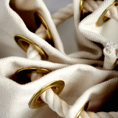Tough white cotton rope strung through large brass grommets, cinching shut an elegant, vintage-inspired ditty bag.