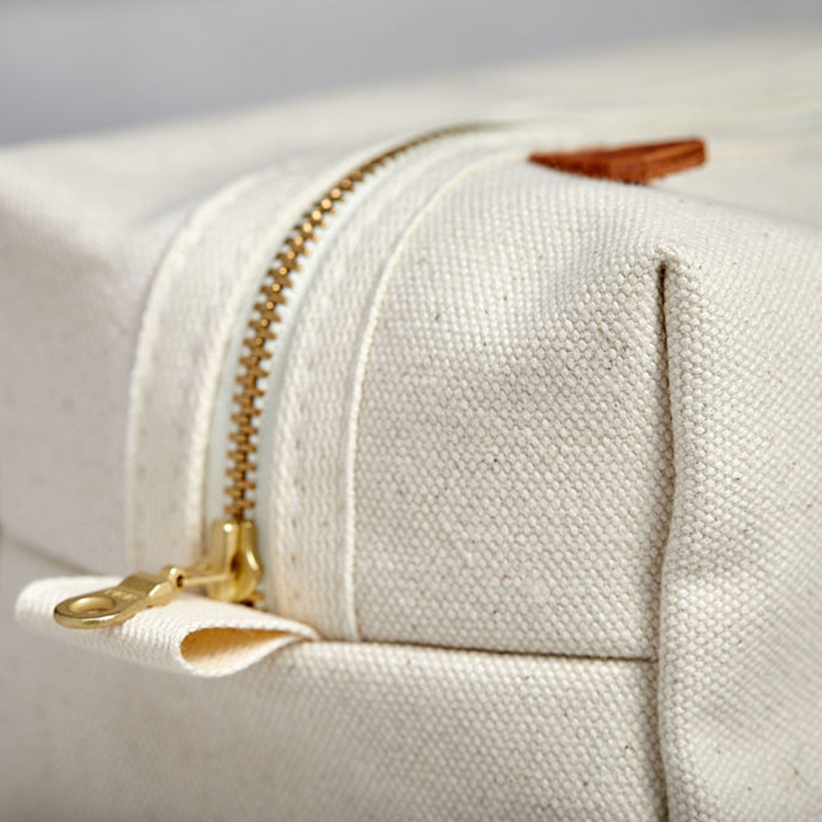 Close-up of end of Dopp kit made from sturdy off-white canvas with metal zipper and leather detail. Classic small travel and toiletry bag.