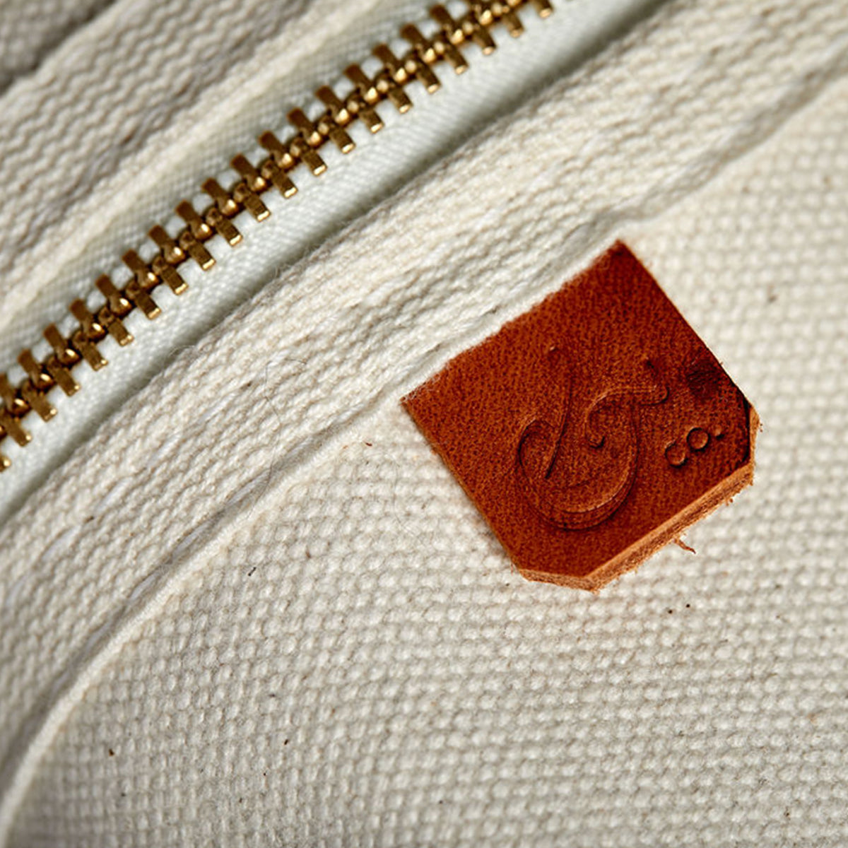 Overhead view of Dopp kit made from sturdy off-white canvas with metal zipper and leather detail. Classic small travel and toiletry bag.