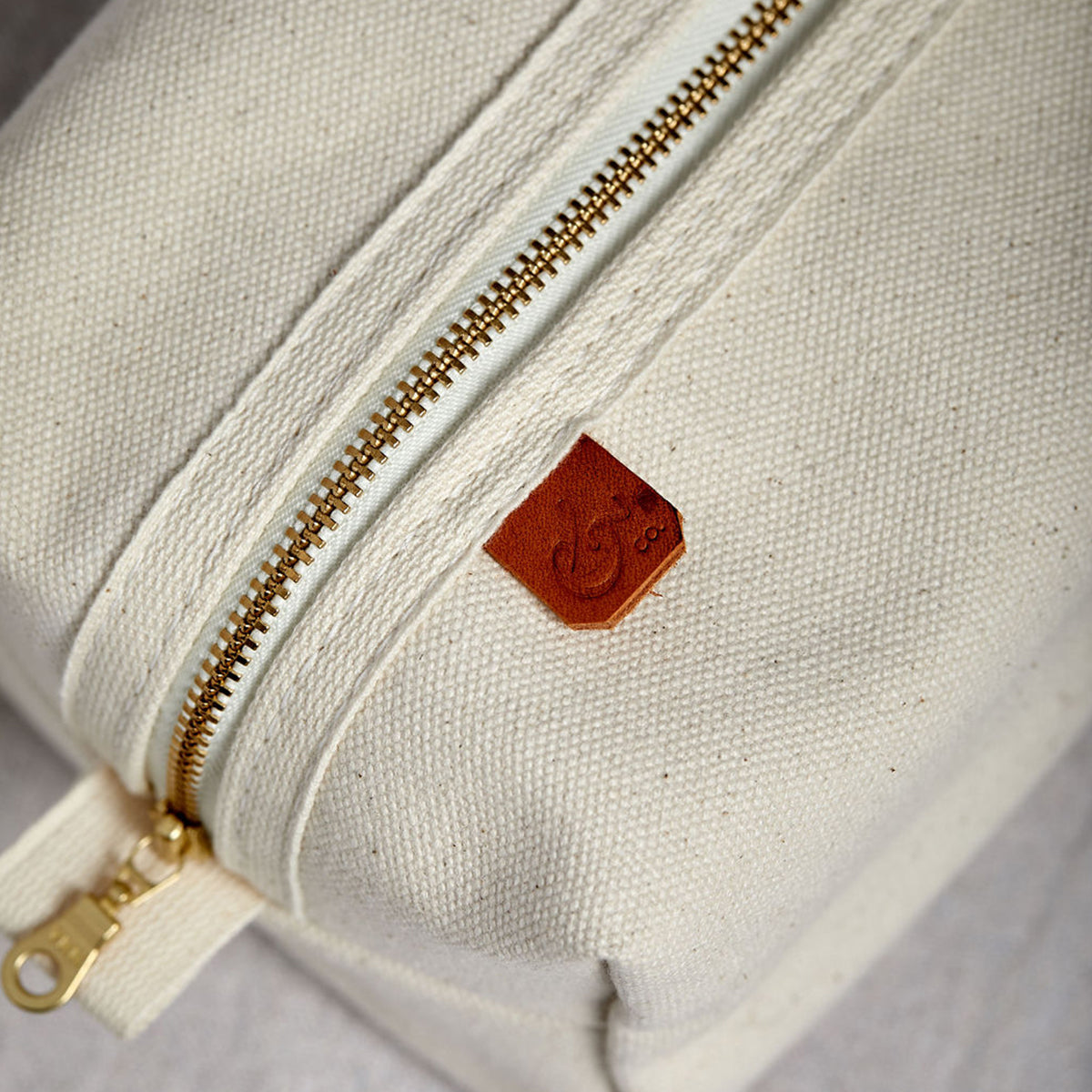Overhead view of Dopp kit made from sturdy off-white canvas with metal zipper and leather detail. Classic small travel and toiletry bag.