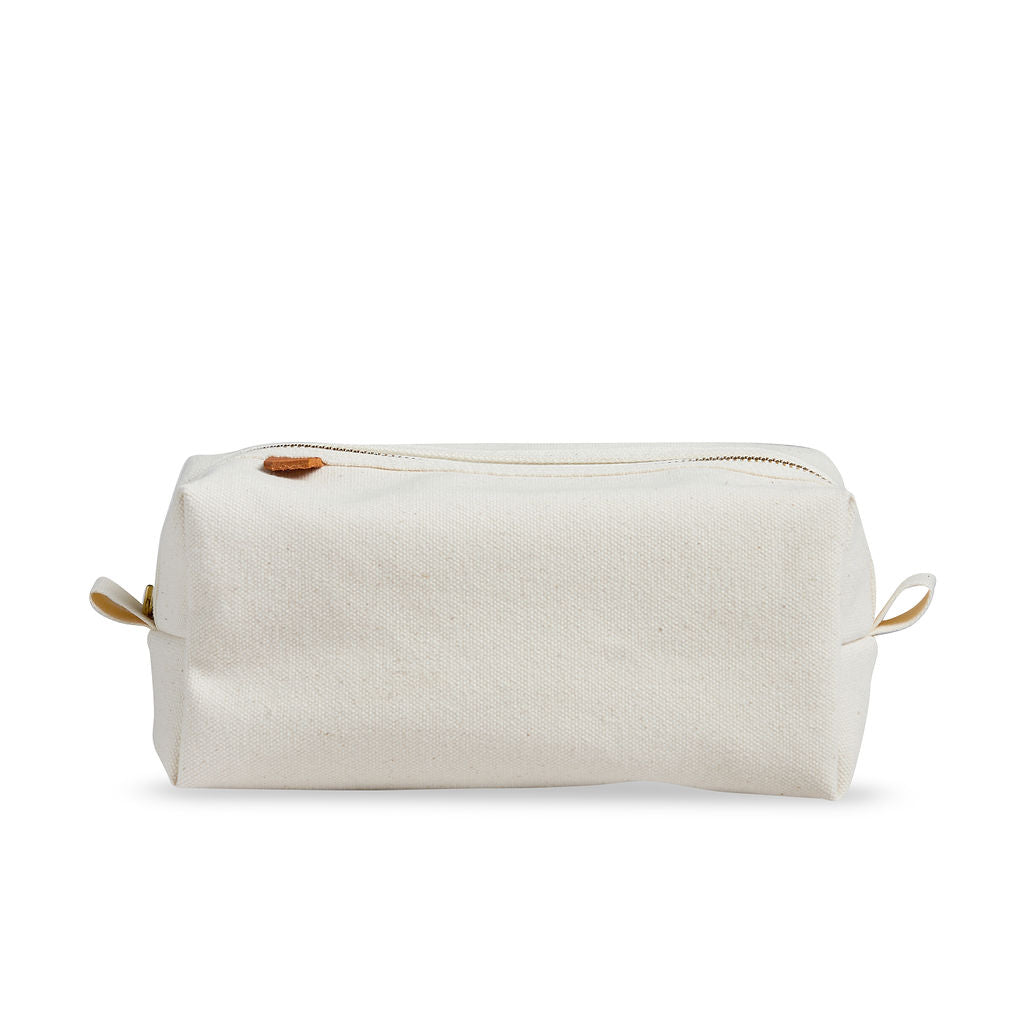 Side view of Dopp kit made from sturdy off-white canvas with metal zipper and leather detail. Classic small travel and toiletry bag.