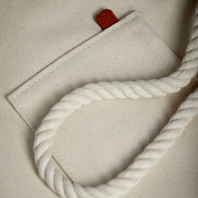 Close-up detail of minimalist, maritime-inspired canvas tote bag. Thick cotton rope and handcrafted leather detail with stamped logo.