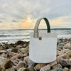 Durable, ultralight white sailcloth bucket bag made from repurposed materials on a beach in Midcoast Maine