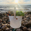 Durable, ultralight white sailcloth bucket bag made from repurposed materials on a beach in Midcoast Maine